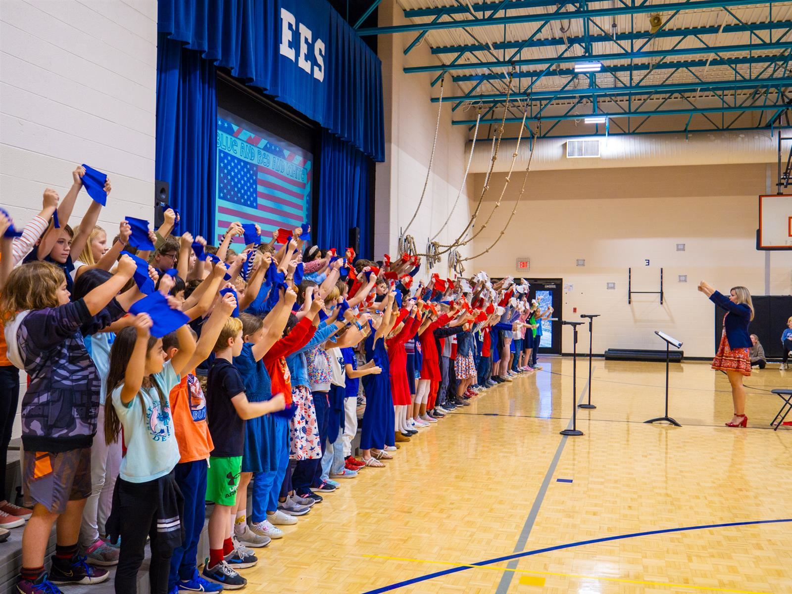 students holding up red, white and blue paper while singing in a choir